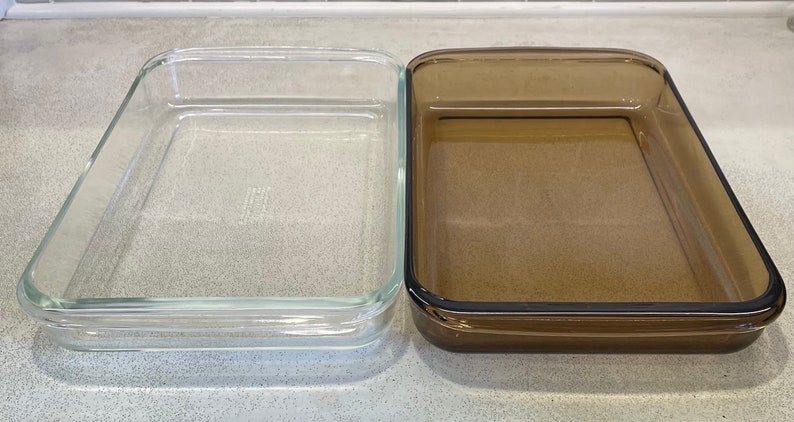 May include: Two rectangular glass baking dishes. One is clear, the other is a brown-tinted glass. Both have a simple, classic design with slightly rounded corners and a raised edge. Ideal for baking casseroles, desserts, or other dishes.