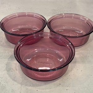 May include: Three purple glass bowls with a ribbed design. The bowls are stacked on top of each other.