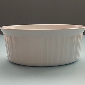May include: White ceramic baking dish with fluted sides. The dish is round and has a smooth, glossy finish.