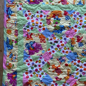 May include: A colorful patchwork quilt with a circus theme. The quilt features various circus animal and clown designs in shades of pink, blue, yellow, and green. The quilt is bordered with a light green and pink trim.