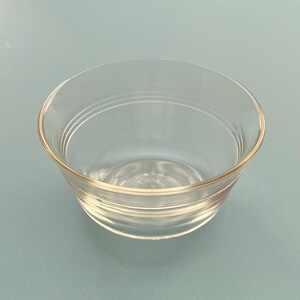 May include: A clear glass bowl with a rounded shape and a slightly flared rim. The bowl has a simple, elegant design with subtle horizontal ridges around the exterior. The glass is transparent, allowing a view of the contents.