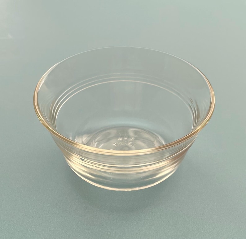 May include: A clear glass bowl with a rounded shape and a slightly flared rim. The bowl has a simple, elegant design with subtle horizontal ridges around the exterior. The glass is transparent, allowing a view of the contents.