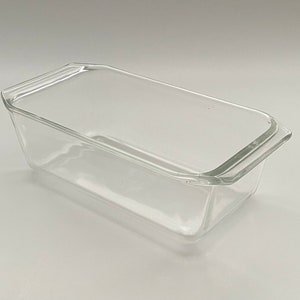 May include: A clear glass loaf pan with a rectangular shape and a lid. The pan has a simple, classic design with a slightly flared rim and handles on each end. Ideal for baking bread or cakes.