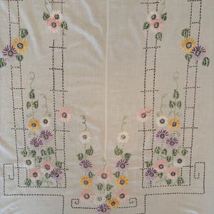 May include: A white fabric textile featuring hand-embroidered black trellis patterns and colorful floral motifs. The design includes yellow, pink, and purple flowers with green leaves arranged in vertical climbing patterns across the surface.