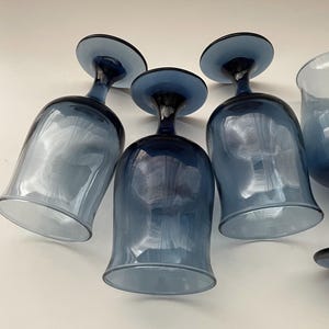 May include: A collection of blue-tinted glass wine glasses. The glasses have a rounded bowl shape and a dark blue stem and base. The glass has a gradient effect, transitioning from a lighter blue at the base to a darker blue at the stem.