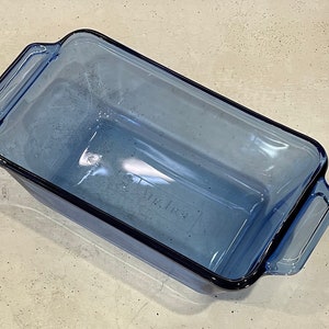 May include: A rectangular, light blue glass baking dish with two handles. The dish has a slightly rounded shape and a dark blue trim. The words "Air Fresh" are visible on the bottom of the dish.