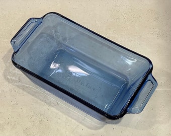 May include: A rectangular, light blue glass baking dish with two handles. The dish has a slightly rounded shape and a dark blue trim. The words "Air Fresh" are visible on the bottom of the dish.