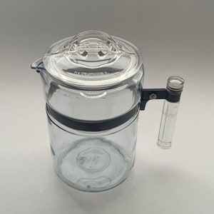 May include: A clear glass coffee pot with a black handle and lid. The lid has a small knob on top and the pot has a black band around the middle. The pot is labeled "Made in USA".