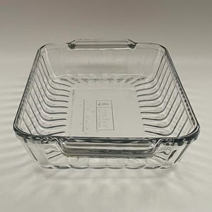 May include: A clear, square glass baking dish with ribbed sides and handles. The dish has the brand name "Anchor" printed on the bottom. The dimensions are 9 x 13 inches.