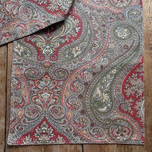 May include: Paisley patterned fabric in red, green, and beige. The fabric features a detailed design with curved shapes and floral elements. The fabric is likely used for home decor or textiles.