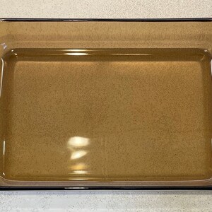 May include: Rectangular amber-colored glass baking dish with rounded corners and a slightly raised rim. The dish is empty and appears clean, suitable for baking or serving. The glass has a speckled appearance.