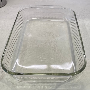 May include: A clear, rectangular glass baking dish with a ribbed design on the sides. The dish has a rectangular shape with rounded corners and handles on each end. Ideal for baking casseroles, desserts, and other dishes.
