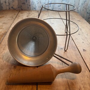 May include: A vintage food mill set consisting of a circular metal strainer with a fine mesh cone, a wire frame stand, and a tapered wooden pestle. The metal components have a matte finish, and the wooden pestle features a smooth, rounded handle.