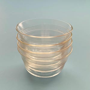 May include: A stack of four clear glass bowls. Each bowl has a rounded rim and a slightly flared shape. The bowls are stacked on top of each other, with the top bowl's rim visible. The glass appears to be smooth and transparent.