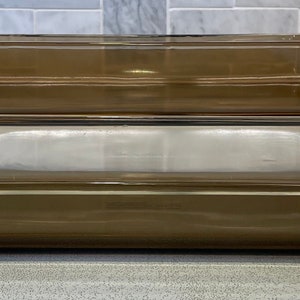 May include: Three rectangular glass baking dishes stacked on top of each other. Two are a transparent brown color, and one is clear. The dishes have a simple, functional design with slightly raised edges and handles.