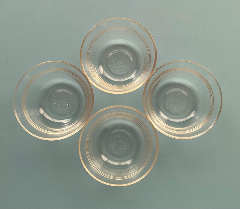 May include: Four clear glass bowls with a circular design. Each bowl has a slightly flared rim and concentric rings around the outside. The bowls are arranged in a square formation against a light blue background.