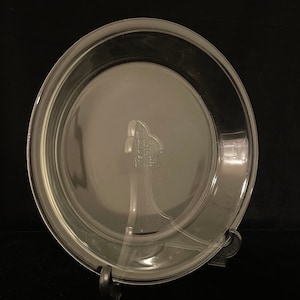 May include: A clear glass pie plate with a raised rim. The plate is 9 inches in diameter and is made of tempered glass.