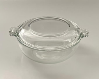 Op de afbeelding: Een heldere glazen ovenschaal met een bijpassende deksel. De schaal heeft twee handvatten en een afgeronde vorm. Het deksel heeft een cirkelvormige inkeping in het midden. De schaal is gemaakt van helder glas.