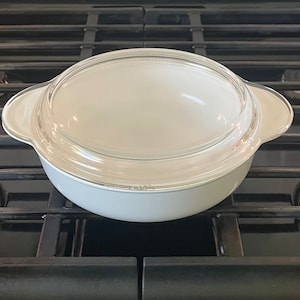 May include: White ceramic baking dish with a glass lid. The dish is sitting on a black stovetop.