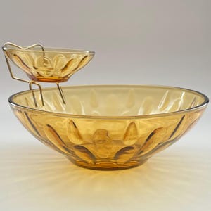 May include: Amber-colored glass serving bowl set with a smaller bowl suspended above it by a metal stand. The bowls have a decorative pattern. The set is designed for serving snacks or dips.