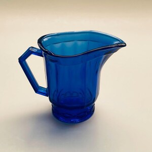May include: A cobalt blue glass pitcher with a fluted design and a handle.