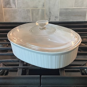 May include: Oval, light blue casserole dish with a clear glass lid. The dish has vertical ribbed sides and a clear glass knob on the lid. The dish is sitting on a black stove top.