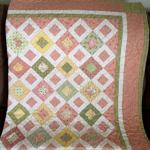 May include: A handmade quilt with a diamond pattern in shades of pink, green, yellow, and white. The quilt features floral and patterned fabric squares, with a decorative border and intricate stitching.