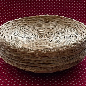 May include: A stack of woven, round, light-colored wicker plates. The plates are stacked on top of each other, with a visible spiral pattern in the center of each plate. The background is a red fabric with white star patterns.