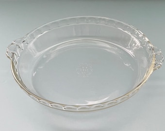 May include: A clear glass pie dish with a fluted edge and two handles. The dish is made by Pyrex and has the text "Pyrex" and "Made in USA" on the bottom.