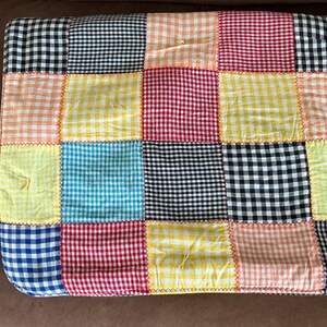 May include: A patchwork quilt featuring a variety of gingham patterns in a range of colors, including black, white, red, yellow, blue, and peach. The squares are stitched together with contrasting thread, creating a vibrant and textured design. The quilt is likely made of cotton.