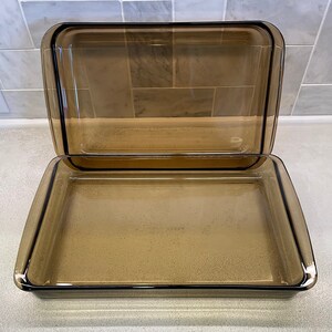 May include: A rectangular, amber-colored glass baking dish with a matching lid. The dish and lid have a simple, classic design, perfect for baking and serving. The glass is transparent, allowing visibility of the contents.