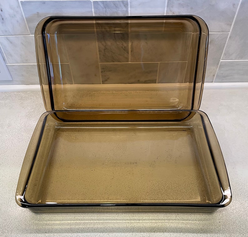 May include: A rectangular, amber-colored glass baking dish with a matching lid. The dish and lid have a simple, classic design, perfect for baking and serving. The glass is transparent, allowing visibility of the contents.