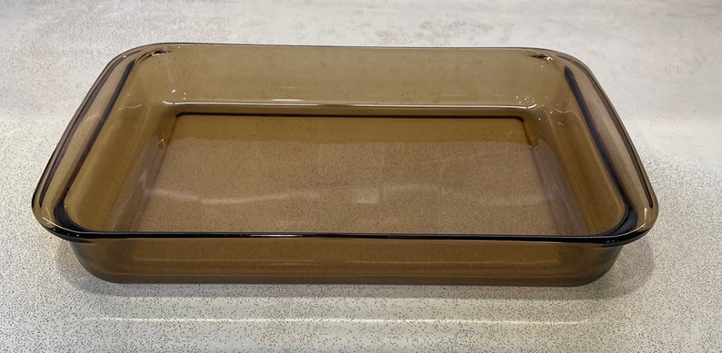 May include: A rectangular, amber-colored glass baking dish. The dish has a simple, classic design with slightly rounded corners and a smooth surface. It is empty and ready for use in the oven.