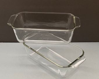 May include: Two clear glass Pyrex loaf pans stacked on top of each other. Each rectangular pan has a slightly flared rim and handles on the short sides. The pans are transparent, allowing a view of the interior.