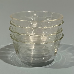May include: Four clear glass bowls stacked on top of each other. Each bowl has a scalloped rim and a ridged design around the sides. The bowls are transparent, allowing light to pass through, and are set against a light blue background.