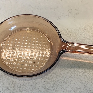 May include: A brown glass frying pan with a textured bottom and a long handle.
