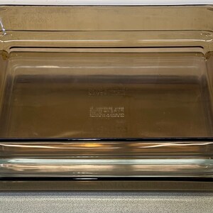 May include: Three rectangular, clear glass baking dishes stacked on top of each other. The dishes have a slightly tinted brown color. The bottom of the middle dish has the text "PYREX" and "MADE IN USA" imprinted.