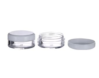 May include: Three clear plastic containers with white lids. The containers are small and round, and the lids are flat. The containers are empty.