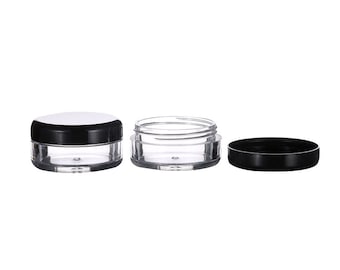 May include: Three clear plastic containers with black lids. The containers are round and have a smooth surface. The lids are flat and have a smooth surface.