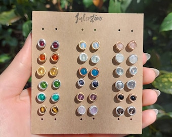 May include: A display card with 18 pairs of gemstone earrings. The earrings are arranged in three columns, each with six pairs of earrings. The earrings are made with different gemstones, including red, orange, yellow, green, blue, purple, and brown. The card is labeled "Jmberstone".