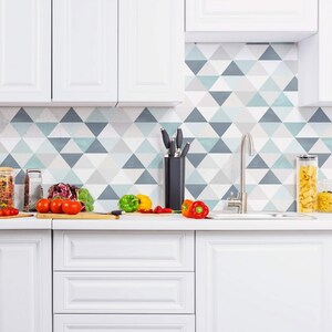 May include: White kitchen cabinets with a white countertop and a sink. The backsplash is a geometric pattern of blue and gray triangles. There are vegetables and a grater on the counter.