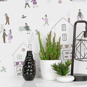 May include: A white ceramic vase with a textured surface holds a small green cactus plant. The vase is sitting on a white surface in front of a white wall with a whimsical hand-drawn pattern of houses, people, and birds.
