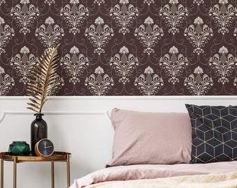 May include: A bedroom with a brown damask patterned wallpaper, a bed with a pink duvet and a throw blanket, and a gold side table with a clock and a vase with a gold branch.
