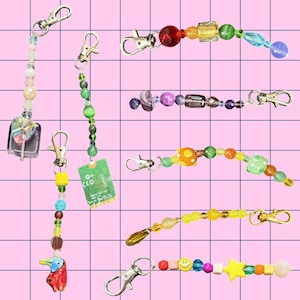 May include: A collection of seven beaded keychains featuring silver-toned lobster clasps. The charms include a square glass heart, a green circuit board, a red bird, and various colorful glass, plastic, and wooden beads in assorted shapes and sizes.