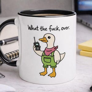 May include: White ceramic mug with a black handle and rim, featuring a cartoon duck in overalls and a pink bandana, holding a walkie-talkie. The text "What the fuck, over." is printed above the duck.