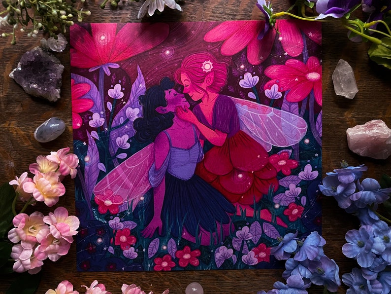 May include: Two fairies with wings, one with dark hair and a purple dress, the other with red hair and a red dress, are embracing in a field of pink and purple flowers. The background is a dark purple with glowing lights.