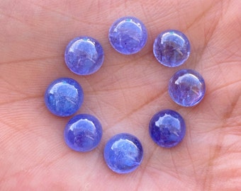 Puede incluir: Ocho cabujones redondos de piedras preciosas azules, probablemente Tanzanita, dispuestos en círculo en una mano.