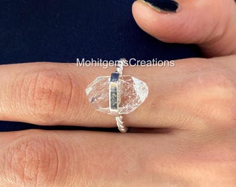 May include: A silver ring with a clear quartz crystal set in a twisted band. The ring is on a finger.