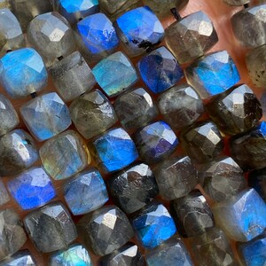 May include: A strand of dark gray faceted labradorite beads with iridescent blue and green flashes. The beads are square shaped and have a polished finish.