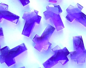 May include: A collection of twelve amethyst crystal crosses, each with a unique shape and size. The crosses are a deep purple color and have a smooth, polished finish.